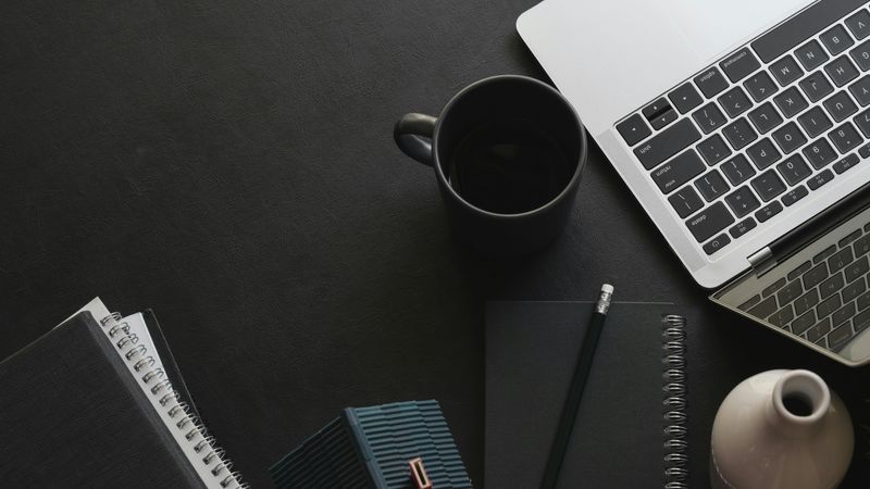 Laptop, coffee mug and notebooks on a dark desk
